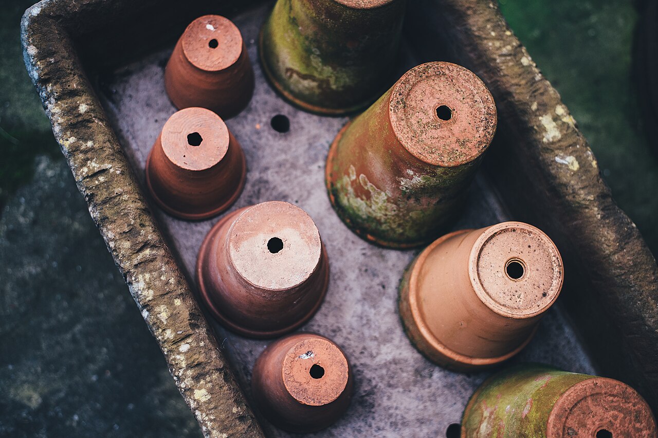Empty, weathered terracotta pots with moss-stained sides turned upside down in a stone trough, drainage holes facing up